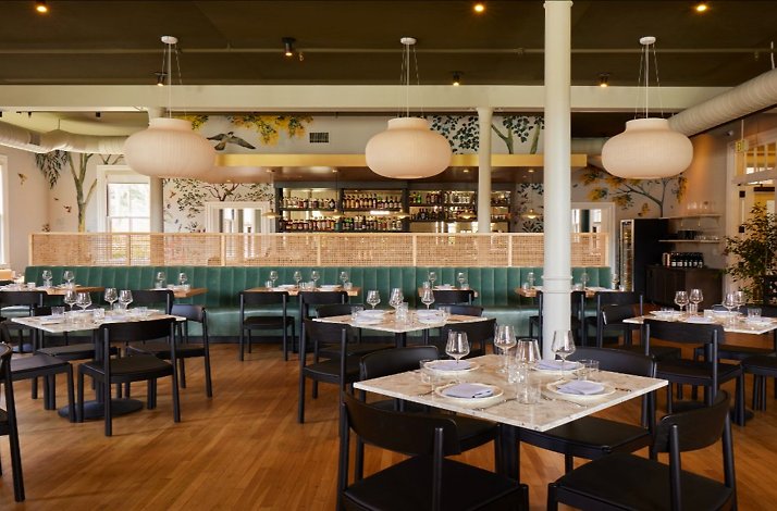 Bright restaurant dining room with marble-topped tables, green velvet banquettes at Dalida restaurant. 
