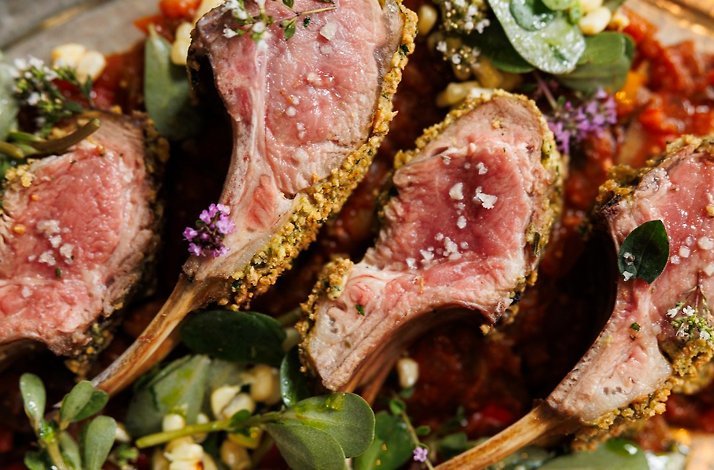 Sliced herb-crusted lamb chops arranged over a bed of greens and tomato ragout, finished with edible flowers and sea salt.