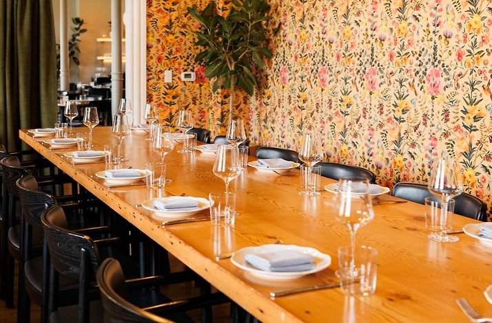 Long wooden communal table set with wine glasses and folded napkins at Dalida restaurant.