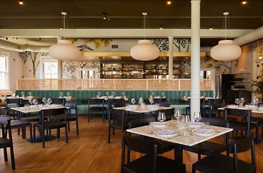 Bright restaurant dining room with marble-topped tables, green velvet banquettes at Dalida restaurant. 