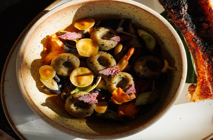 Sunlit bowl of herb dumplings and mushrooms with a charred slab of grilled meat on the side at Maria Isabel.