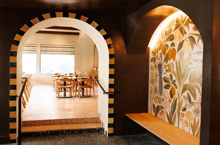 Arched entryway leading into a bright dining room with warm wood tables and chairs at Maria Isabel.