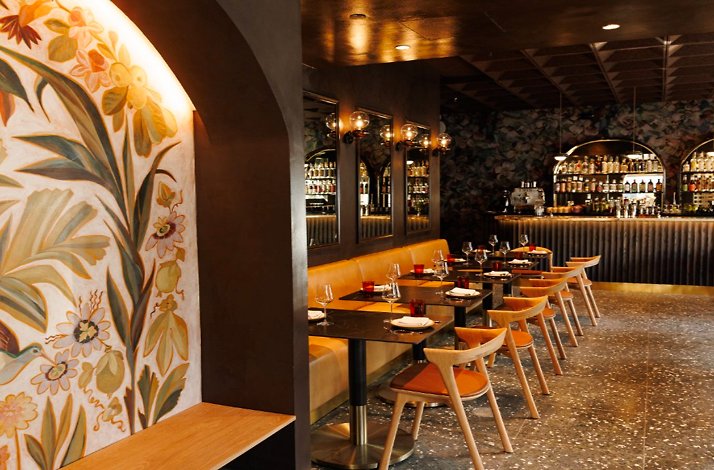 Moody dining room with floral wall mural, candlelit tables, and a curved back bar lined with bottles at Maria Isabel.