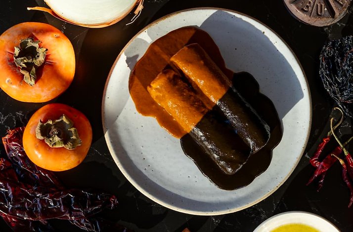 Two mole-coated tamales plated with persimmons and dried chiles in a dramatic overhead spread at Maria Isabel.