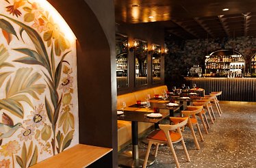 Moody dining room with floral wall mural, candlelit tables, and a curved back bar lined with bottles at Maria Isabel.