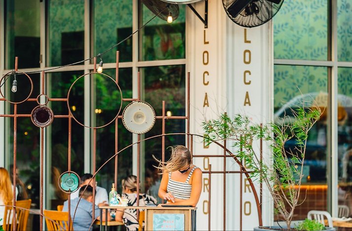 Outdoor dining area at L'Oca d'Oro restaurant, with guests seated, string lights, rustic metal decor on the facade. 