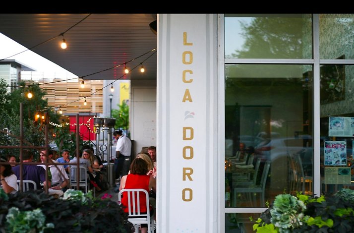 Outdoor patio seating with string lights and the L’Oca d’Oro sign on the building column.