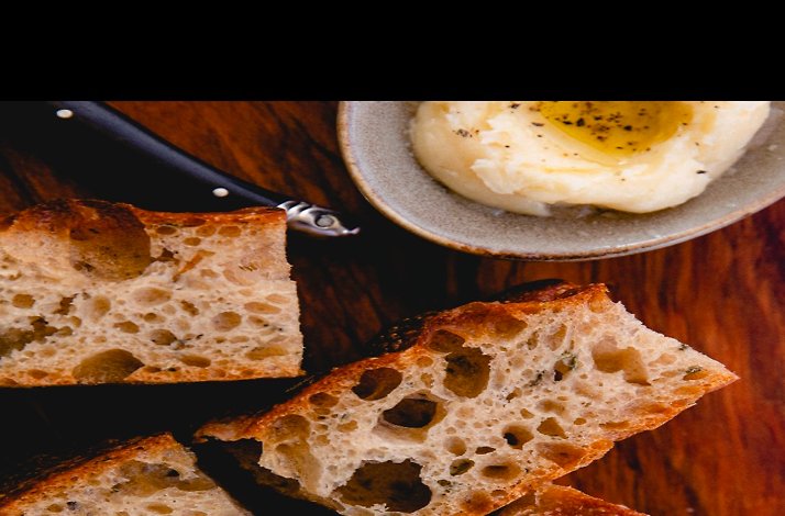 Rustic sliced bread with whipped butter and olive oil on a wooden table served at L’Oca d’Oro.