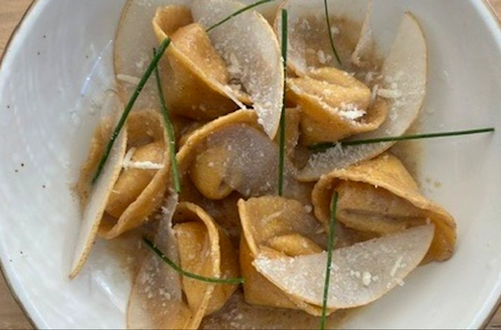 Stuffed pasta parcels in golden broth, topped with shaved cheese and chive garnishes, served in a white ceramic bowl.
