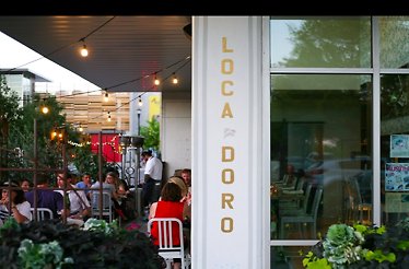 Outdoor patio seating with string lights and the L’Oca d’Oro sign on the building column.