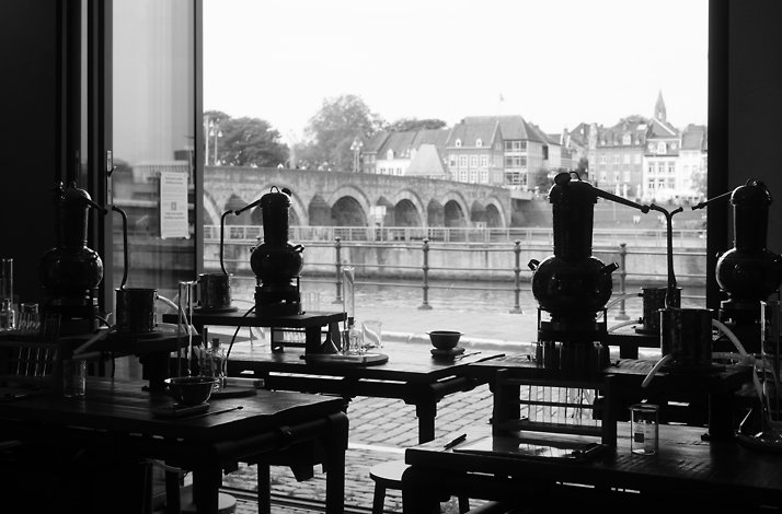 City Distillery Maastricht workshop space with copper gin stills on tables, overlooking the Sint Servaasbrug bridge and Maas river.