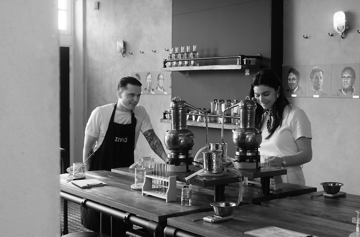 ZIVIO-aproned instructor and guest smiling beside copper gin stills during a hands-on distilling workshop at City Distillery Maastricht.