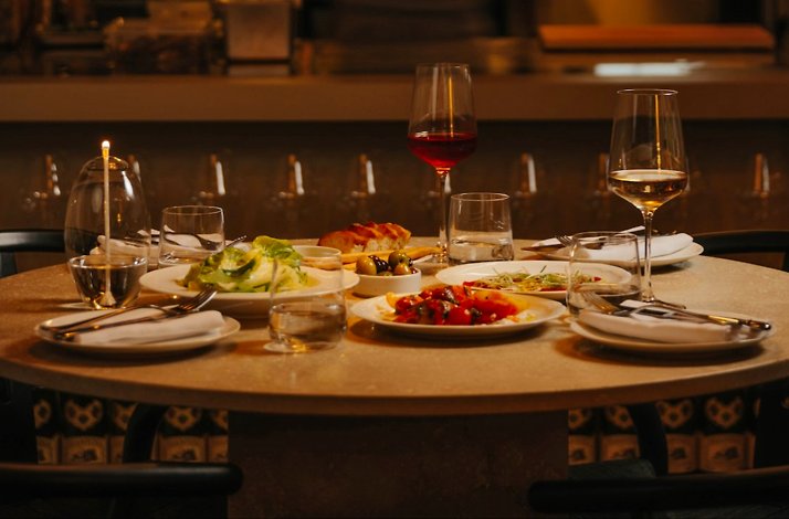 Candlelit restaurant table featuring shared appetizer plates, wine glasses, and water glasses arranged for a dinner.