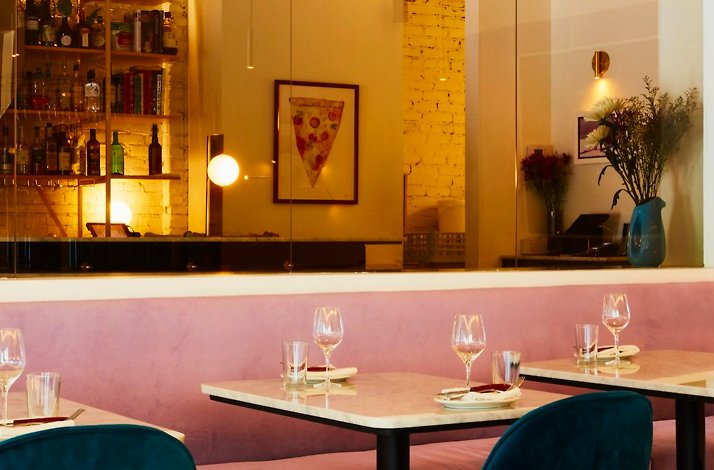 Cozy restaurant dining area with pink banquette seating, marble tables, and warm ambient lighting at Elena Restaurant. 