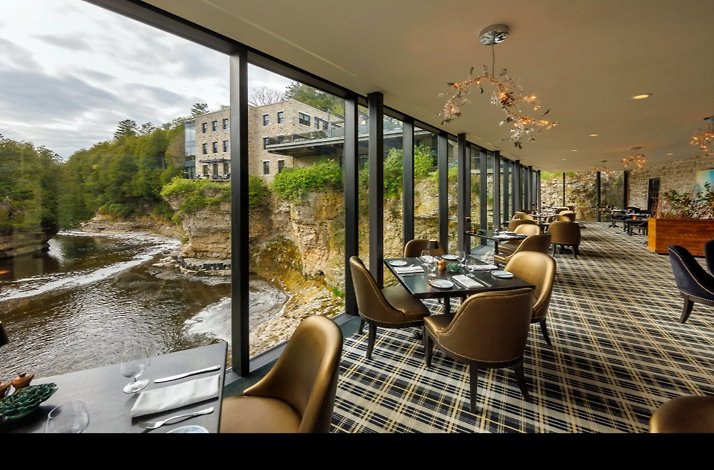 Elora Mill Hotel dining room with floor-to-ceiling windows overlooking the Grand River, Elora Gorge, and stone hotel building. 