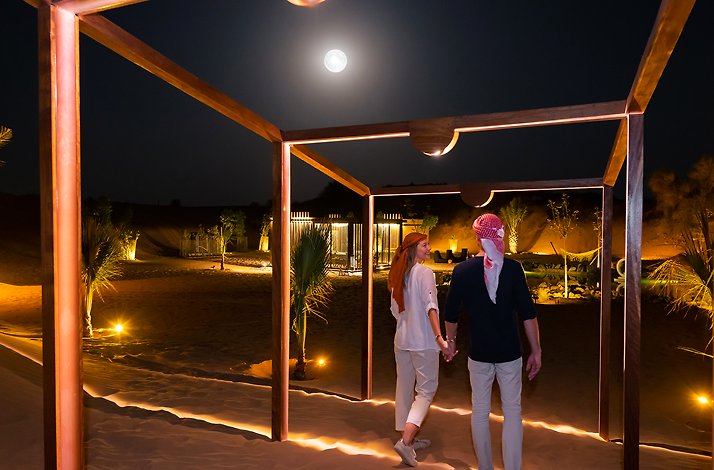 A happy couple walking through a wooden arch bathed in the light of a full moon.